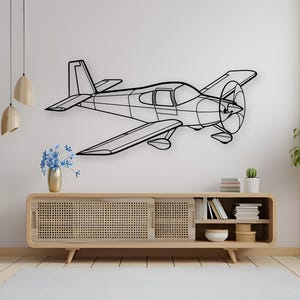 May include: A black metal airplane wall art piece. The outline of the plane is visible, including the wings, propeller, and tail. The artwork is mounted on a white wall above a wooden cabinet. The room is decorated with plants and a rug.