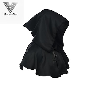 May include: A black hooded capelet featuring a smooth fabric construction with a pointed hood and a front closure secured by a black ribbon tie. A small black cross pendant hangs from the ribbon tie. The logo Historium Vault is visible.