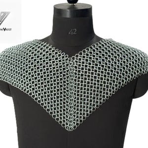 May include: A silver-colored chainmail mantle featuring a V-shaped neckline and interlocking metal rings. The piece is displayed on a black mannequin torso. The Historium Vault logo is visible in the upper left corner of the image.