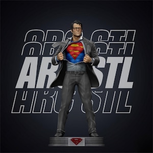 Pode incluir: Estátua do Superman de terno, revelando o icônico emblema "S" no peito. A figura está em uma base com o logotipo do Superman. O fundo é preto com texto branco.