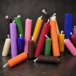 May include: A collection of colorful, cylindrical candles with a honeycomb pattern. The candles are in various colors, including brown, green, pink, yellow, red, orange, blue, purple, and cream. Each candle has a white wick.
