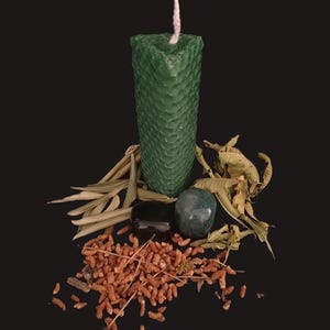 Peut inclure: Une bougie triangulaire en cire d'abeille vert foncé avec une texture en nid d'abeille et une mèche blanche, accompagnée de deux pierres polies lisses, un tas de petits éléments botaniques séchés bruns et plusieurs longues feuilles séchées.
