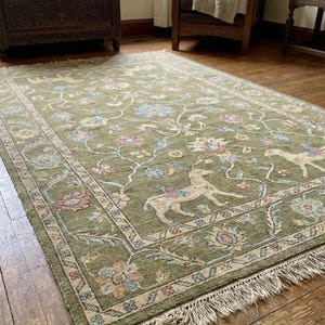 May include: A rectangular green rug with a floral and deer pattern. The rug has a cream-colored border and fringe. The design includes blue, pink, and cream-colored flowers and deer.