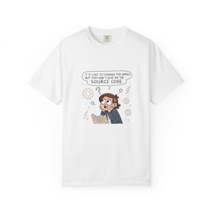 Op de afbeelding: Wit T-shirt met een cartoon illustratie. Het ontwerp toont een personage dat nadenkt over een boek, omringd door tandwielen, vraagtekens en bliksem. Tekst luidt: "I'D LIKE TO CHANGE THE WORLD, BUT THEY WON'T GIVE ME THE SOURCE CODE."