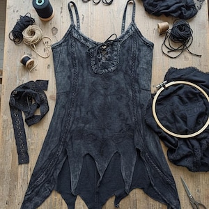 Puede incluir: Un top de camisola negro bordado con escote con cordones y tirantes finos, rodeado de suministros de costura como carretes de hilo, encaje y tijeras, todo dispuesto sobre una superficie de madera.