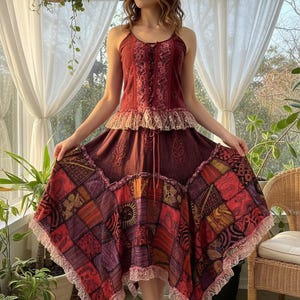 Peut inclure: Une robe bordeaux à col licou avec une jupe patchwork. Le corsage présente des détails en dentelle et un cordon de serrage. La jupe est composée de carrés à motifs variés en rouge, orange et violet, bordés de dentelle.