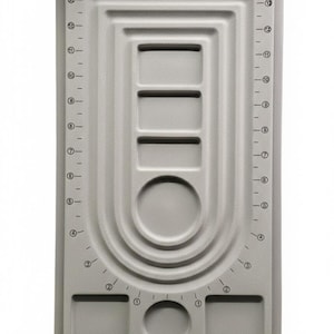 Peut inclure: Un tapis de craft rectangulaire gris avec des zones encastrées et une règle sur les côtés. Le tapis comporte des encoches rectangulaires et circulaires, avec des mesures en centimètres. Idéal pour la création de bijoux et autres travaux manuels.