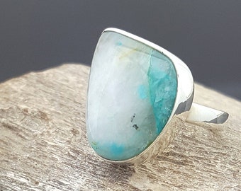 May include: A silver ring with a light blue and white gemstone. The ring is set on a piece of wood.