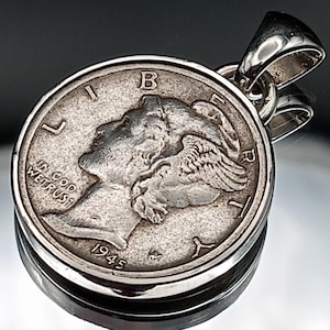 Puede incluir: Colgante de plata con una moneda de diez centavos Mercury de 1945. La moneda está engastada en un bisel de plata con un lazo para una cadena. La moneda muestra el perfil de una mujer con un gorro alado. Las palabras "IN GOD WE TRUST" son visibles.