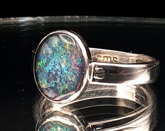 May include: A silver ring with a round, dark green opal gemstone. The ring has a simple band and the opal has a dark green, blue, and black color.
