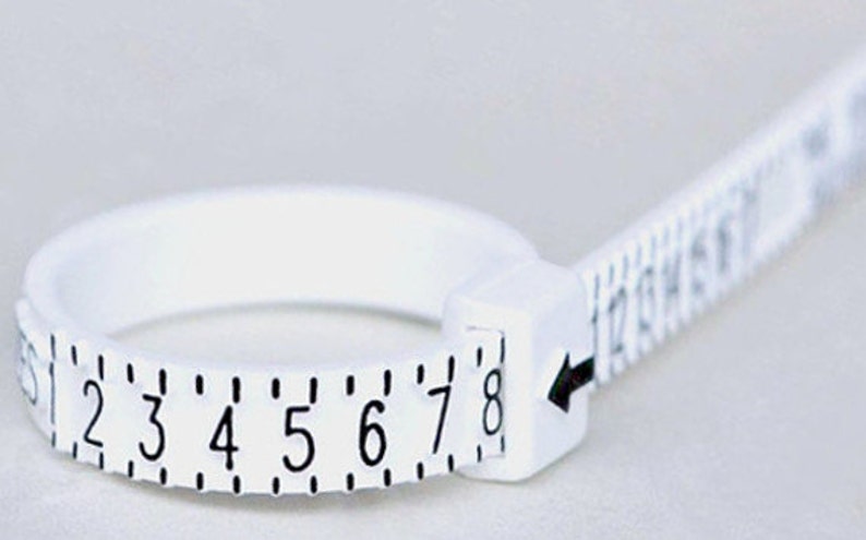May include: White plastic ring sizer with a measuring tape attached. The ring sizer has numbers 1 through 8 printed on it. The measuring tape has numbers 12 through 18 printed on it.