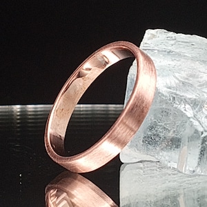 Puede incluir: Una banda de boda de oro rosa cepillado con un borde ligeramente redondeado.