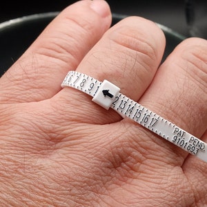 May include: White plastic ring sizer with black numbers and an arrow pointing to the size 13. The text "PAT. PEND. 9101693" is printed on the sizer.