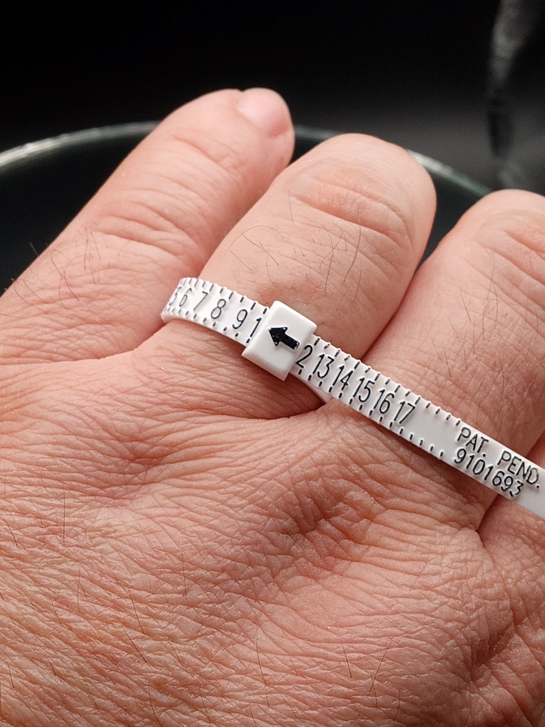 May include: White plastic ring sizer with black numbers and an arrow pointing to the size 13. The text "PAT. PEND. 9101693" is printed on the sizer.