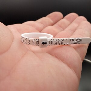 May include: White plastic ring sizer with black markings for sizes 6 through 17. The sizer has a black arrow pointing to the right and the text "PAT. PEND. 9101693".