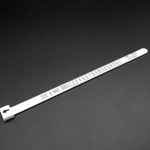 May include: White plastic ring sizer with black markings for sizes 1 to 17. The sizer has the text "SIZE & HALF SIZES 1 2 3 4 5 6 7 8 9 10 11 12 13 14 15 16 17" and "PAT. PEND. 6910161" printed on it.