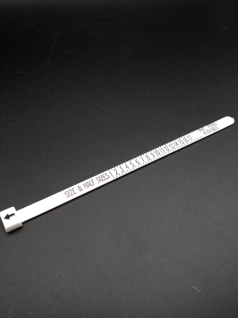 May include: White plastic ring sizer with black markings for sizes 1 to 17. The sizer has the text "SIZE & HALF SIZES 1 2 3 4 5 6 7 8 9 10 11 12 13 14 15 16 17" and "PAT. PEND. 6910161" printed on it.