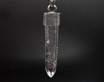 May include: A clear quartz crystal pendant on a silver chain. The crystal is faceted and has a pointed tip. The pendant is attached to a silver bail.