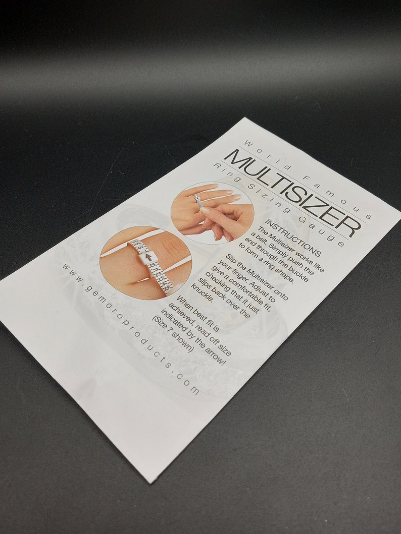 May include: White plastic ring sizer with a buckle and a measuring tape. The Multisizer works like a belt. Simply push the end through the buckle to form a ring shape. Slip the Multisizer onto your finger. Adjust to give a comfortable fit, checking that it just slips back over the knuckle. When best fit is achieved, read off size indicated by the arrow! (Size 7 shown).