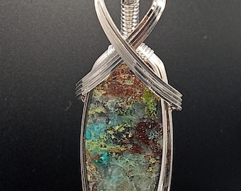 May include: A silver wire wrapped pendant featuring a green, blue, and brown stone with a heart-shaped bail.