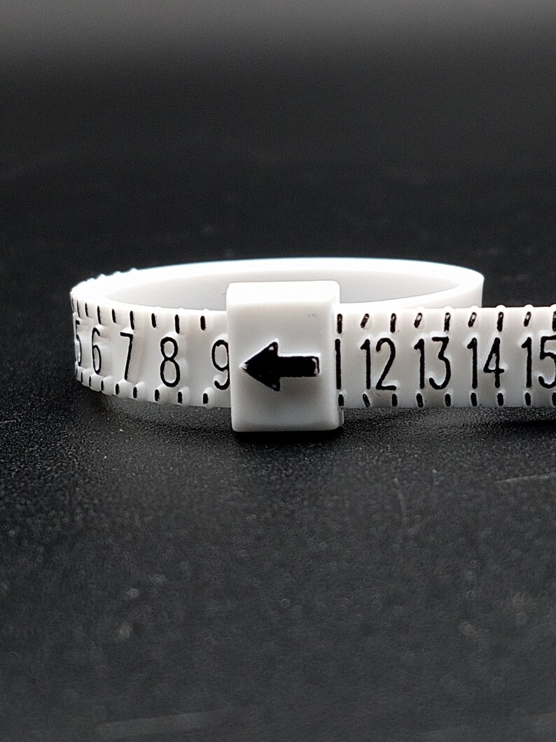 May include: White plastic ring sizer with black numbers 6 through 15 and an arrow pointing to the left.