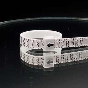 May include: White plastic ring sizer with black numbers and arrows. The numbers range from 4 to 17.