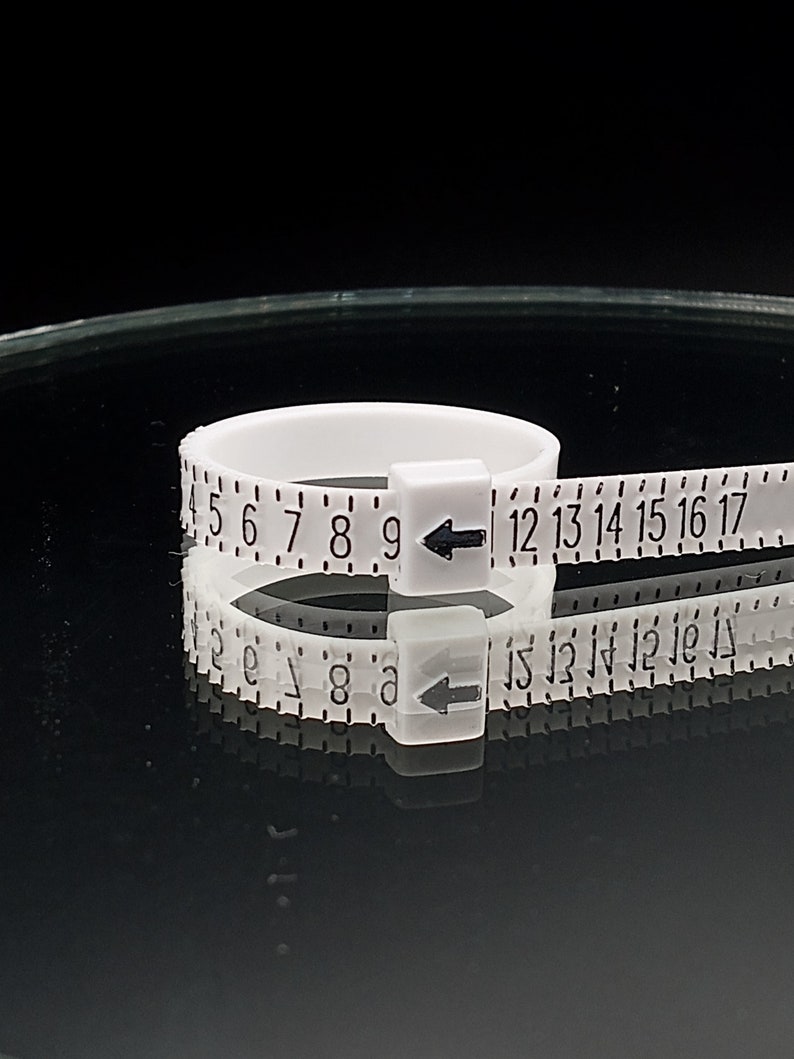 May include: White plastic ring sizer with black numbers and arrows. The numbers range from 4 to 17.