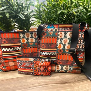 Peut inclure: Ensemble de sacs et pochettes à motifs. Les motifs présentent un mélange de motifs géométriques orange, rouge, marron et sarcelle. L'ensemble comprend un sac fourre-tout, un sac bandoulière avec une sangle noire et deux petites pochettes.