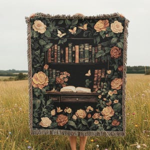 Puede incluir: Una manta de tapiz negro con un diseño de estantería, rosas y mariposas. La manta tiene un borde con flecos y se sostiene en un campo. Las rosas son en tonos de amarillo, melocotón y crema. Mide aproximadamente 150 cm x 180 cm.