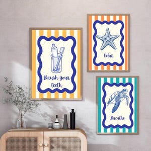 Puede incluir: Tres impresiones artísticas enmarcadas con temática costera. Cada impresión presenta una ilustración azul y blanca sobre un fondo crema, con los textos "Brush your teeth", "Relax" y "Breathe". Los marcos tienen un patrón de rayas.