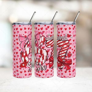 Puede incluir: Tres vasos térmicos rosas con patrones de corazones y los números "Six" y "Seven" en rojo y blanco. Cada vaso tiene una pajita plateada y una tapa. El diseño incluye lazos y corazones.