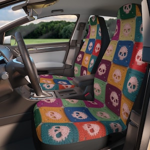 Puede incluir: Un par de fundas para asientos de coche con un colorido patrón de ganchillo de calaveras de color rosa claro sobre fondos cuadrados de color amarillo, azul, rojo, morado, naranja y verde. Las fundas están puestas en los asientos delanteros.