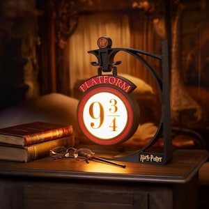 Peut inclure: Lampe signe Platform 9 3/4 noire et rouge avec un design circulaire, avec les chiffres 9 3/4 dans une lumière vive. La lampe est soutenue par un support noir et porte les mots "Harry Potter" à la base.