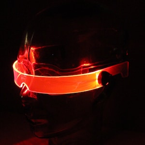 Può includere: Un cerchietto luminoso rosso a LED con una cornice in plastica trasparente. Il cerchietto è indossato su una testa di manichino.