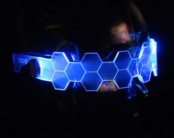 May include: A pair of blue LED light-up glasses with a hexagonal design. The glasses are worn on a mannequin head.