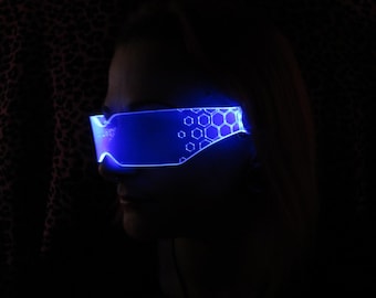 May include: A person wearing blue, glowing, futuristic-style glasses with a hexagonal pattern. The glasses are lit up with blue light.
