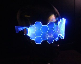 May include: Blue LED light-up glasses with a hexagonal pattern. The glasses are on a black mannequin head.