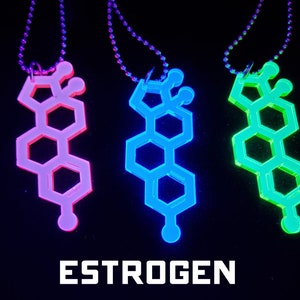 Puede incluir: Tres collares con colgantes que brillan en la oscuridad con forma de la estructura química del estrógeno. Los colgantes son rosa, azul y verde.