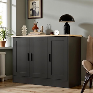 May include: A black cabinet with three doors and a light wood top. A black lamp, a small clock, and decorative items sit on top. A framed black and white portrait hangs on the wall.