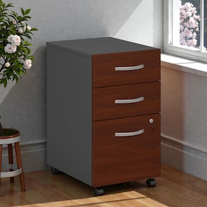 May include: A three-drawer file cabinet with a dark gray frame and cherry-colored drawers. The drawers have silver handles and the bottom drawer has a lock. The cabinet sits on small black wheels.