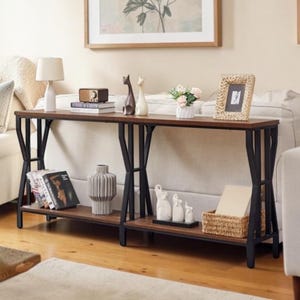 May include: A long, rectangular console table featuring a dark brown wooden top and a lower shelf supported by a black metal frame with geometric side supports. The table holds books, a lamp, vases, figurines, and a woven basket on its surfaces.