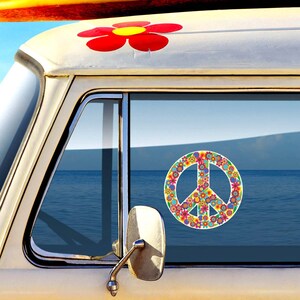May include: A white van with a peace sign sticker on the window. The peace sign is made of colorful flowers. The van is parked in front of a body of water.
