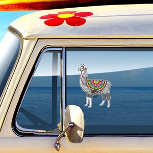 Pu&ograve; includere: Un lama grigio con motivi floreali colorati sulla schiena &egrave; visibile attraverso il finestrino di un furgone vintage. Il furgone ha un adesivo di un fiore rosso sul tetto.