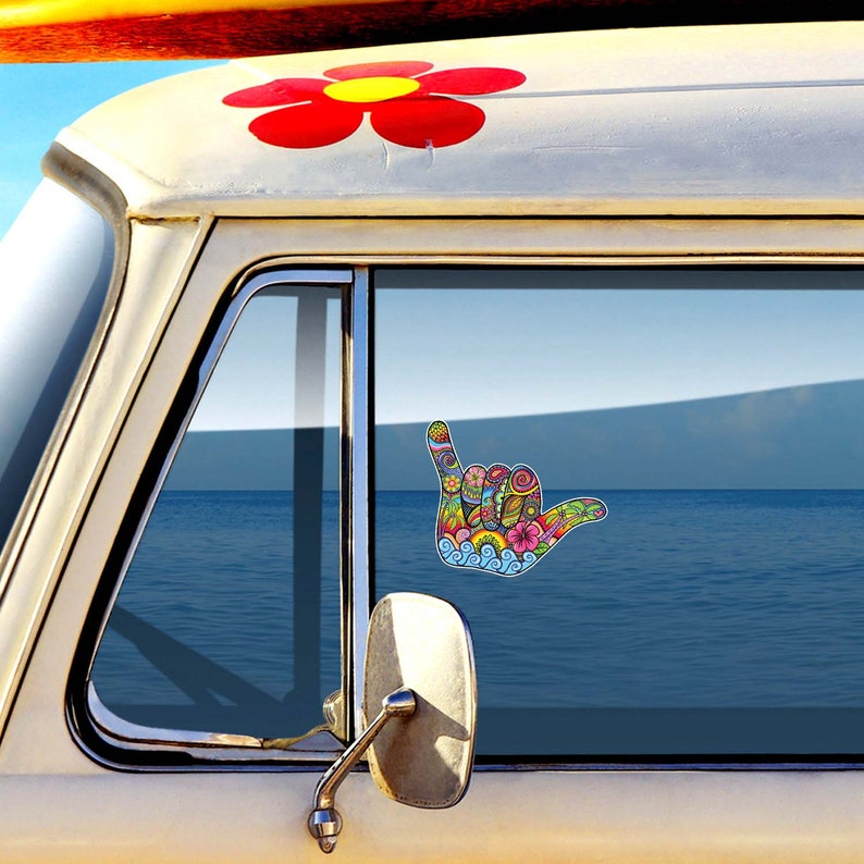 Beautiful hang loose hand artwork on a van window in front of the ocean