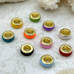May include: A collection of ten colorful enamel beads with gold-tone metal rims. The beads are in various colors, including yellow, green, purple, orange, pink, black, blue, and red. The beads are arranged on a textured, off-white surface.
