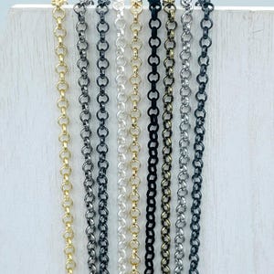 May include: A collection of various metal chain necklaces in gold, silver, black, and gunmetal gray. The chains are displayed vertically, showcasing different finishes and styles of link designs. The background is a light, neutral color.