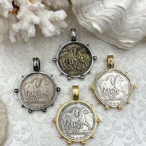May include: Four round pendants with horse imagery. The pendants have silver and gold tones, with a detailed relief of two horses. Each pendant has a loop for a chain. The pendants are displayed on a textured, off-white surface.