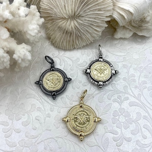 Può includere: Tre pendenti rotondi con motivi a forma di ape. I pendenti sono dorati e argentati, con dettagli intricati. Sono presentati su una superficie bianca strutturata, con elementi di corallo e conchiglie sullo sfondo. Gioielli.
