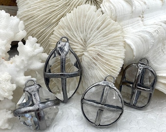 May include: Four clear glass pendants with a dark metal frame. The pendants have different geometric shapes, including teardrop and circular designs. The background features white coral and shell elements.