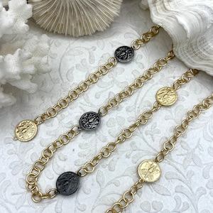 May include: Gold-toned chain necklaces with circular bee-themed pendants. The chains have a chunky link design, and the pendants alternate between gold and black finishes. The necklaces are displayed on a white, patterned surface, suggesting a jewelry or accessory theme.